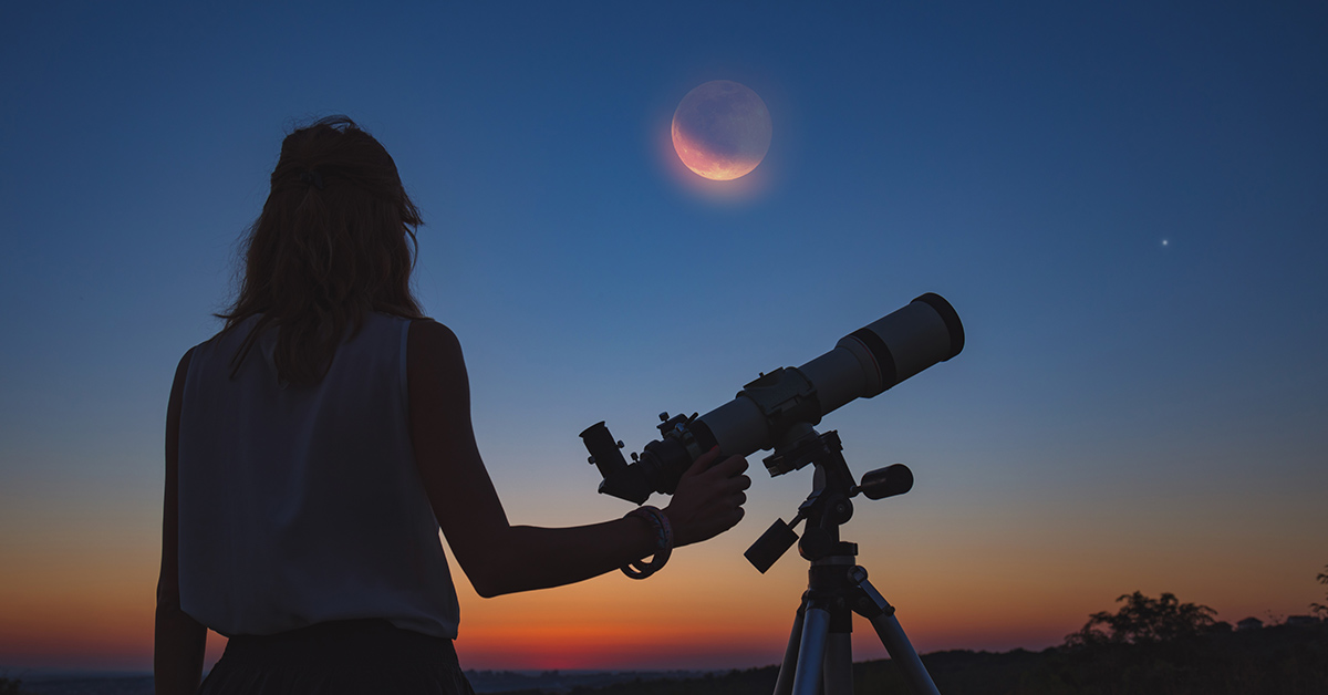 person looking at the moon with a telescope