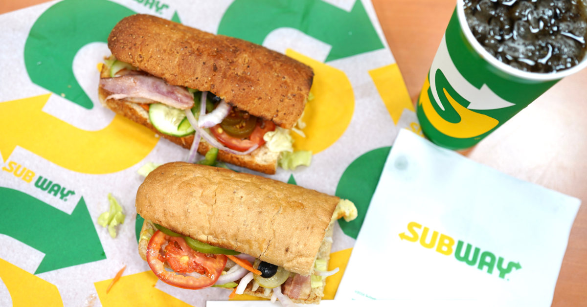 two six inch Subway sandwiches on display with a soda