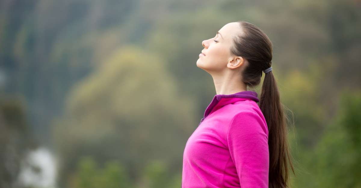 woman wearing pink taking a deep breath outdoors