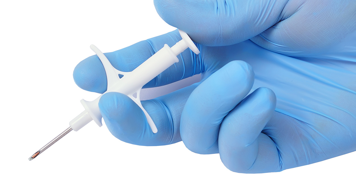 hand with blue latex glove holding a small white syringe
