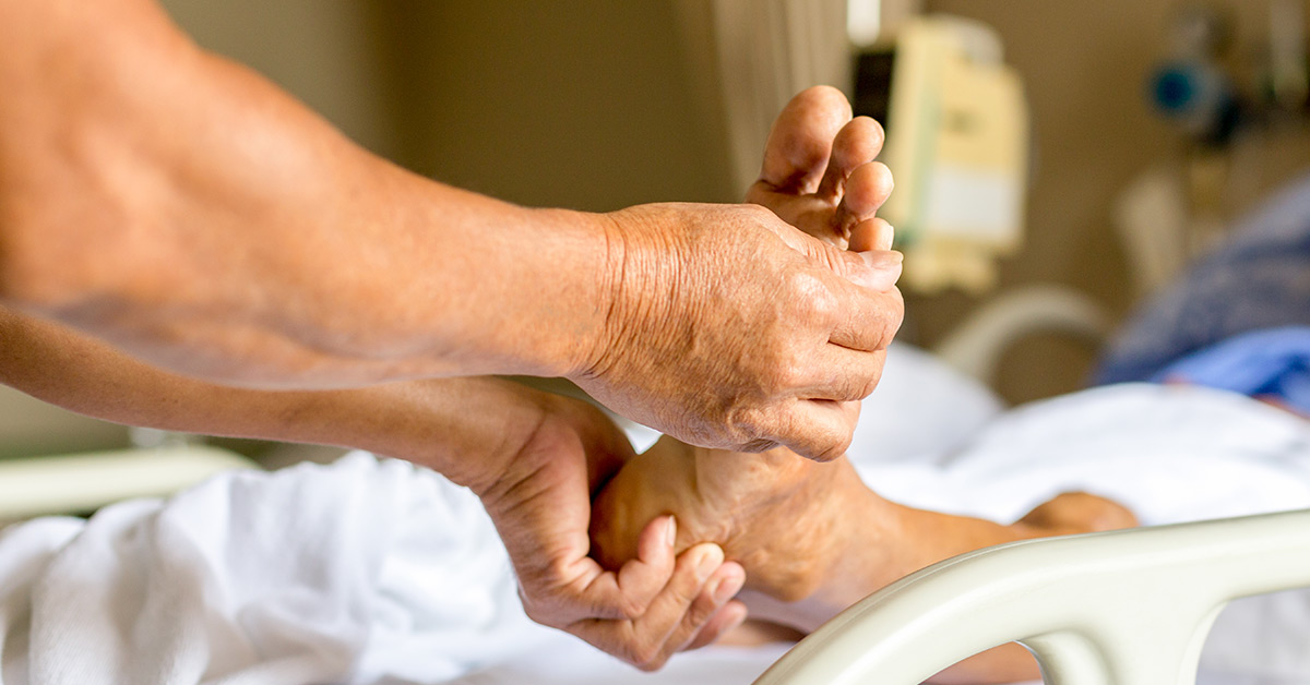 foot of a patient in a hospital bed being examined and held by a pair of hands