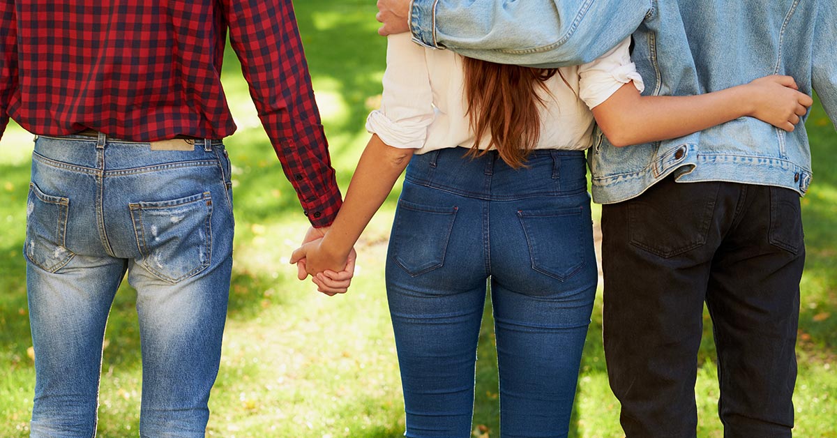 a throuple. female in the centre holding one partners hand while putting her arm around the other.