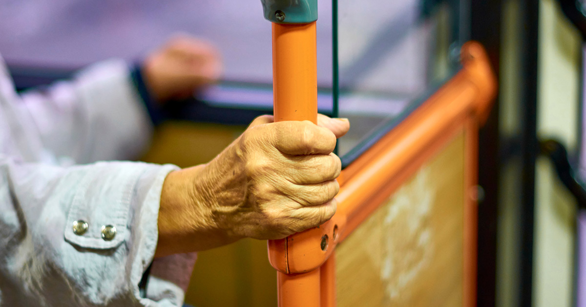elderly womans hand holding on to a pole on public transit