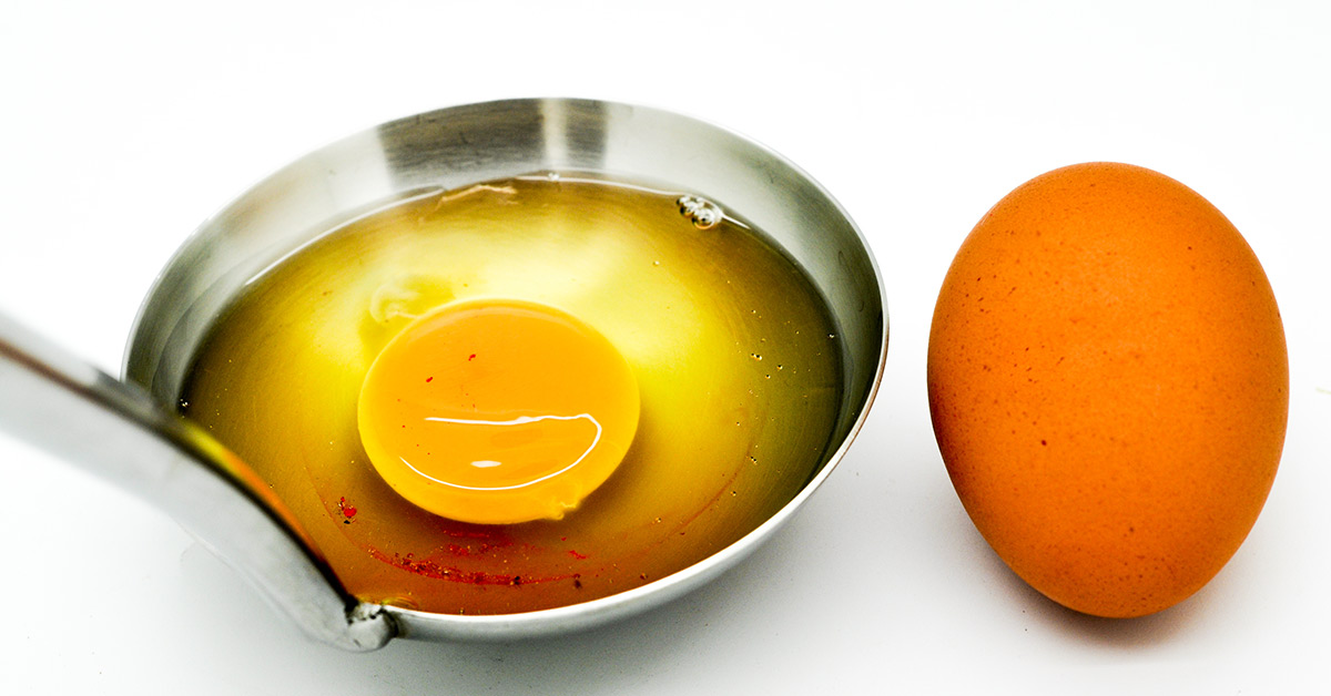 brow egg and an egg cracked into a silver dish with blood spots