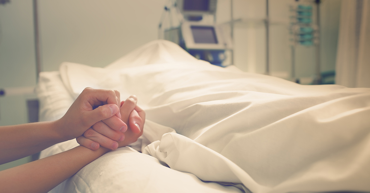 holding the hand of a ill patient in a hospital bed