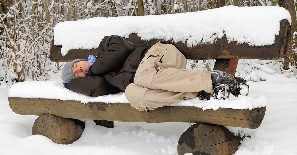 man sleeping on a snow covered bench