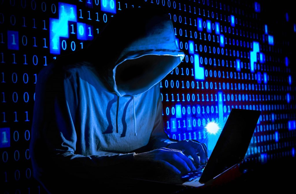 depiction of a hacker wearing a hooded sweater, their face can't be seen. ones and zeros can be seen in the background depicting computer code