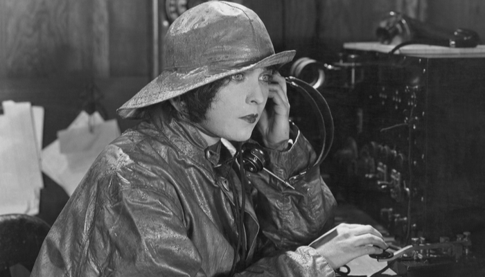 woman sitting at a table wearing a raincoat doing morse code