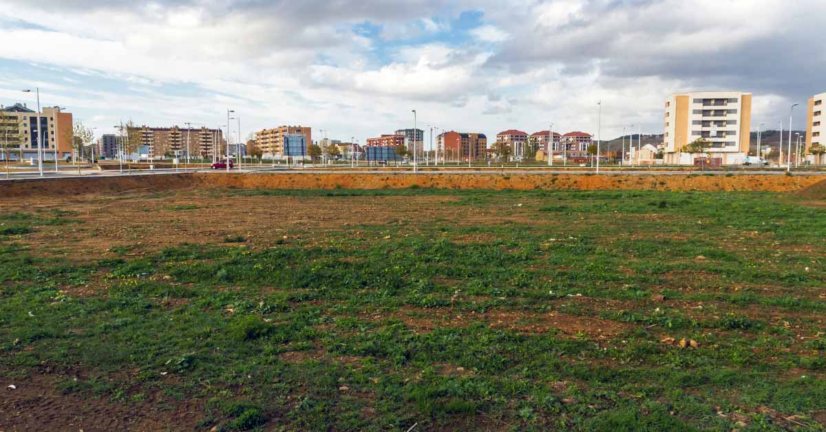 large grassy field with apartment buildings seen in the background
