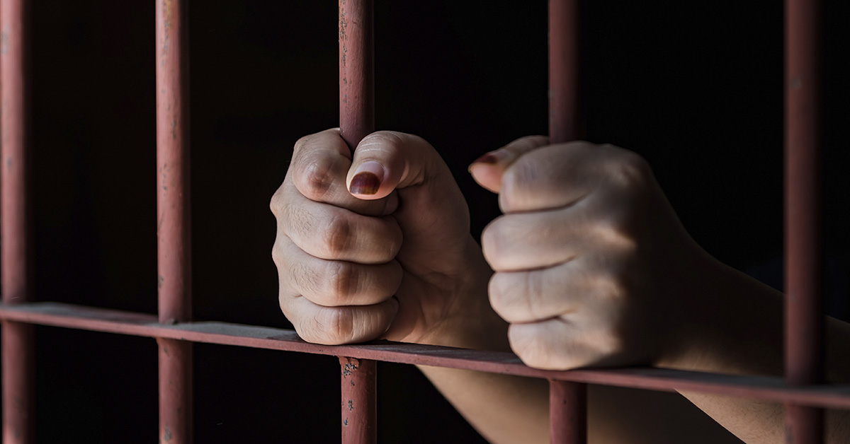 hands holding bars on a jail cell door