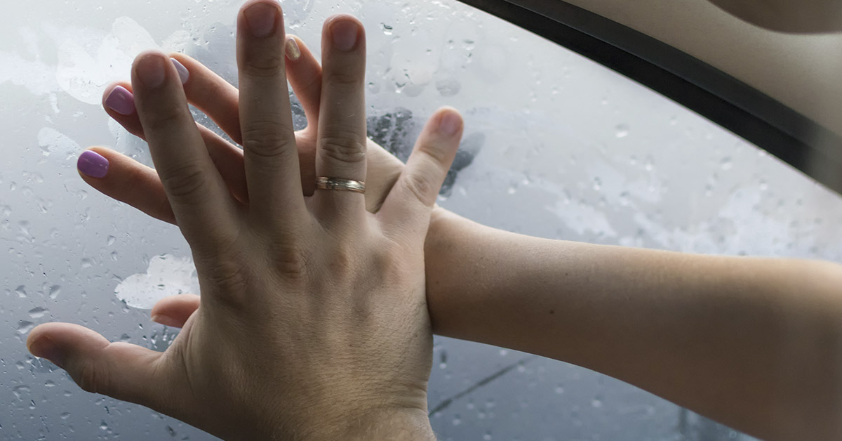 hands placed over one another on a window with condensation