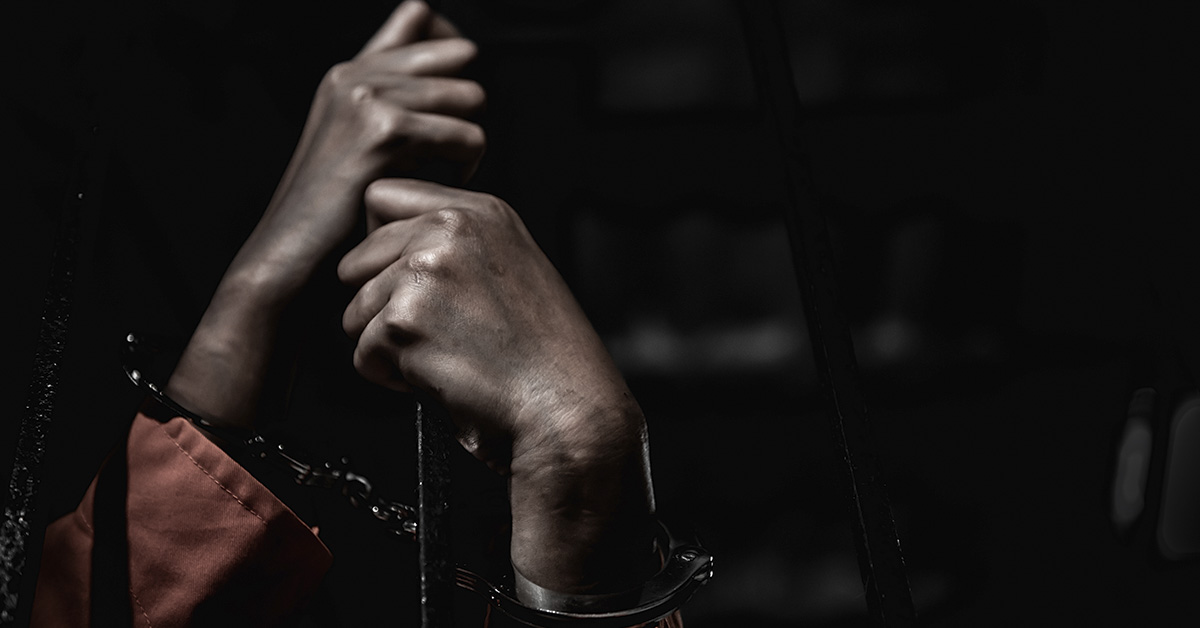 an inmate's handcuffed hands grabbing the rung of a prison door
