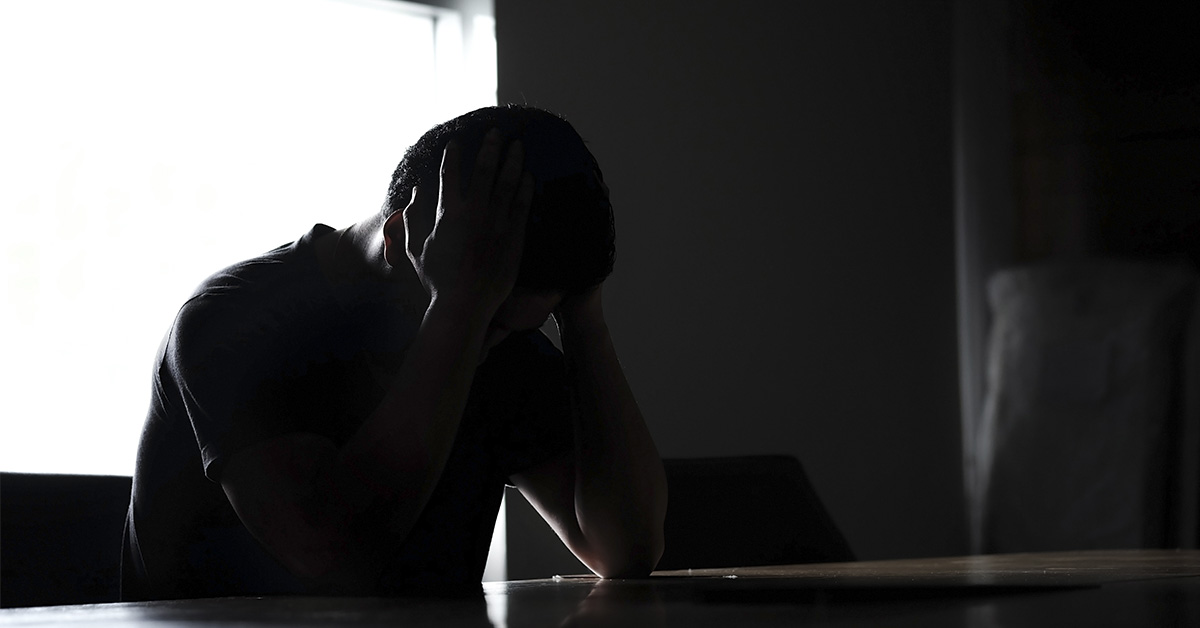 silhouette of sad man sitting at table, hands placed on head