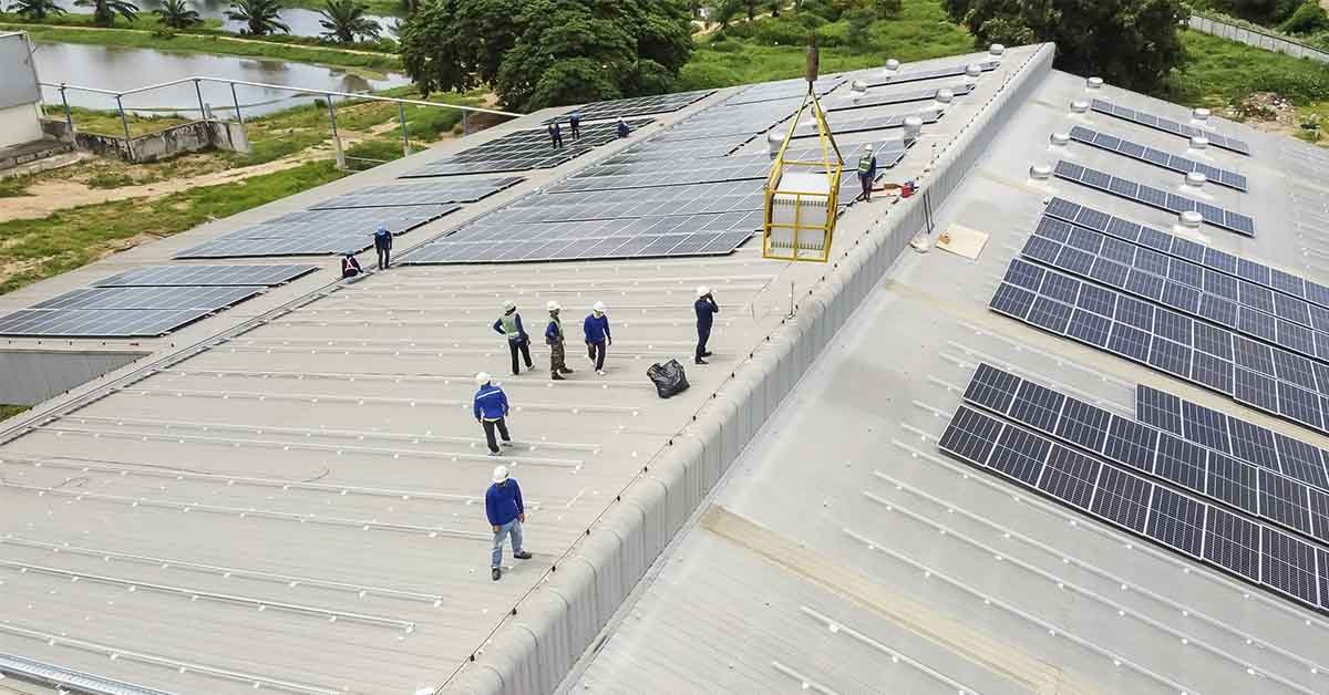 workers installing solar panels on large roof of industrial building