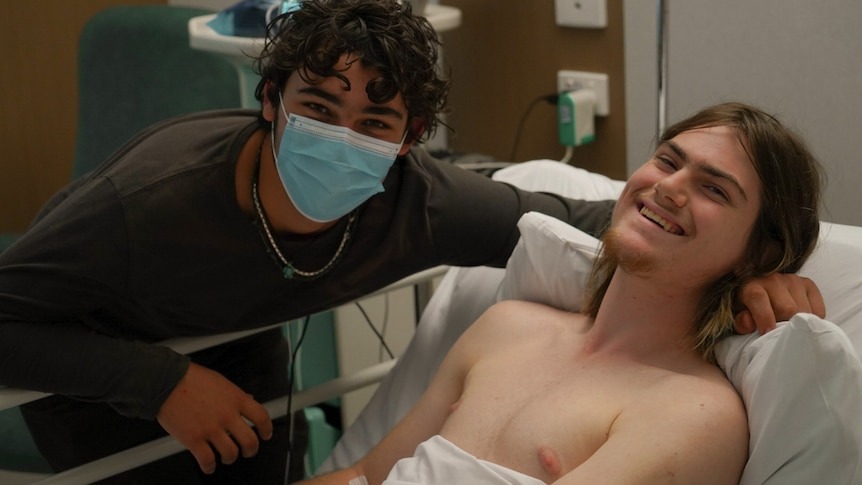 Luke Pascoe (R) recovering from the shark attack. His best friend and savior Conner Shirley (L) looks over him.