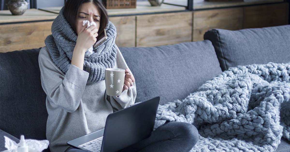 woman sick at home on couch blowing nose