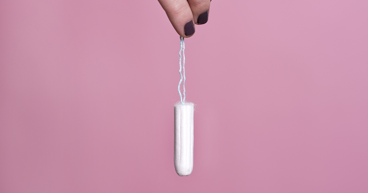 pink background. hand holding tampon by string