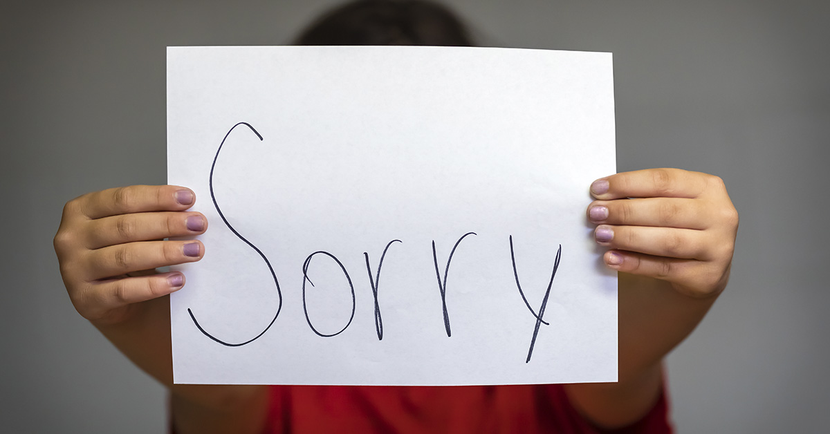 person holding piece of white paper with the word "sorry" written on it