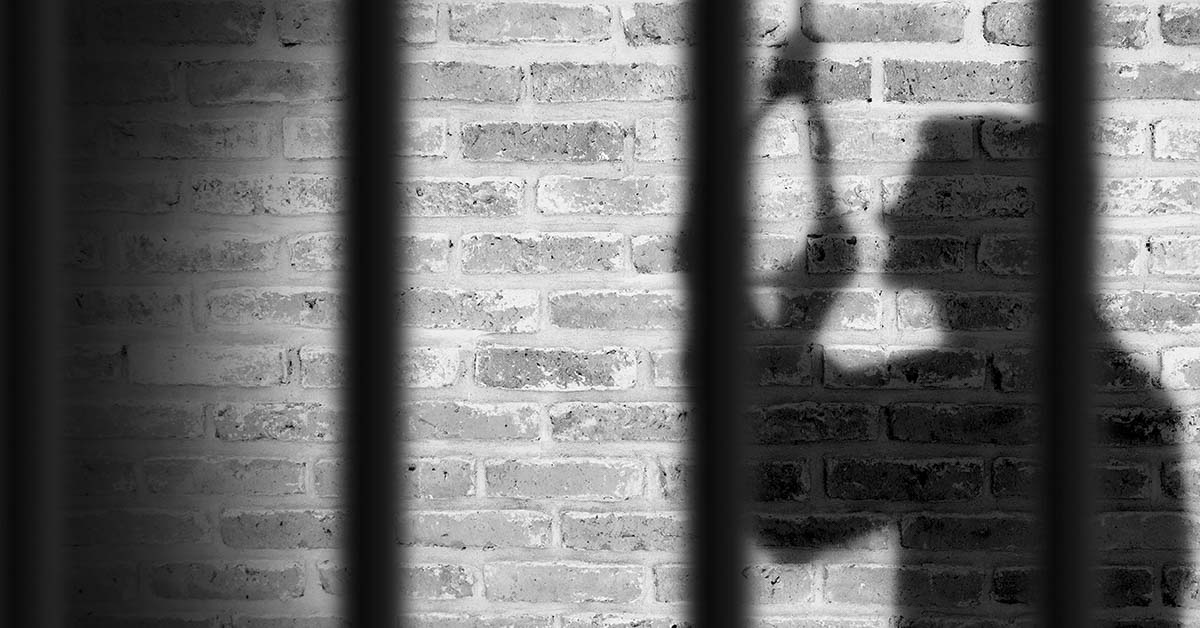 shadow of someone in a jail cell cast on a brick wall. black and white image.