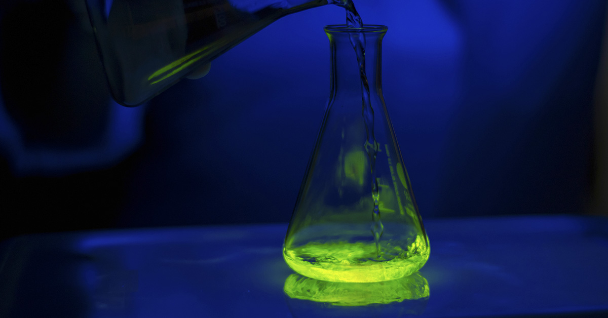neon green liquid being poured into Erlenmeyer Flask