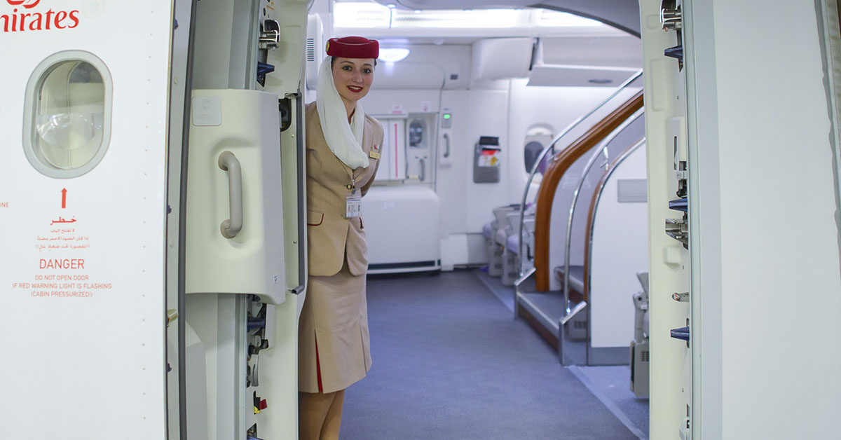 a member of the cabin crew greeting flyers at door of plane