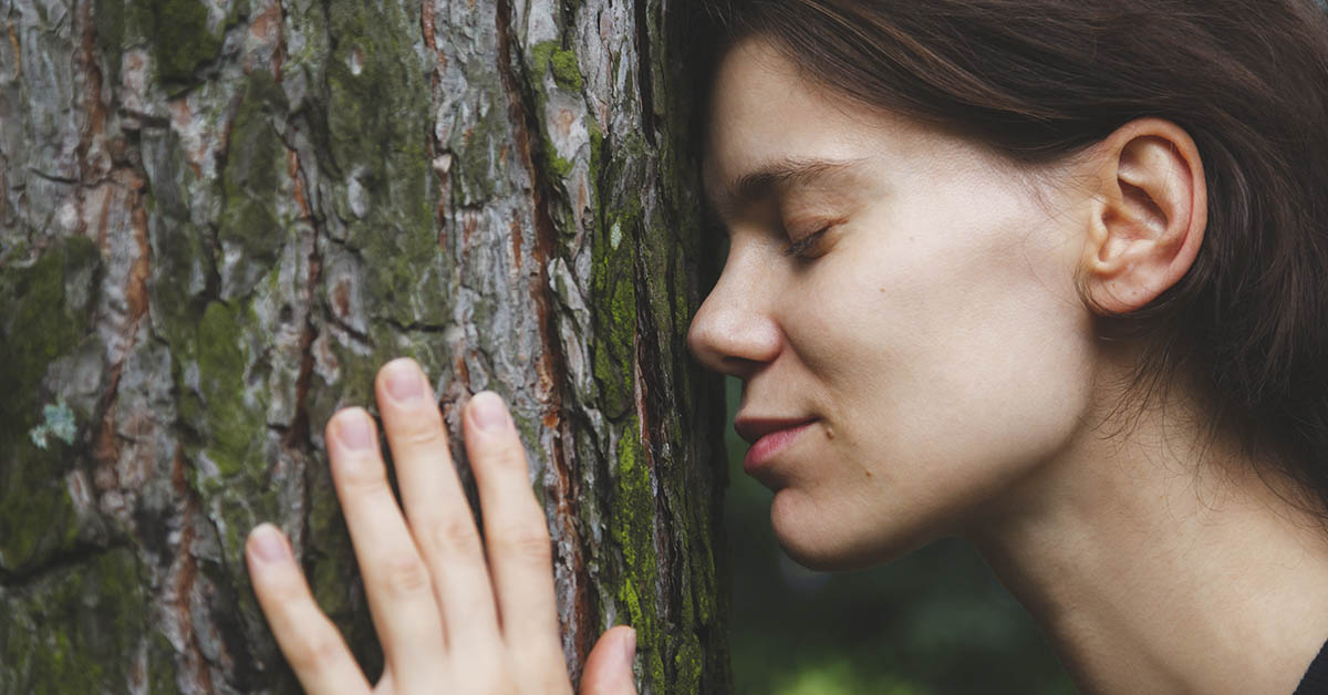 woman embracing and placing her face and hands on a tree