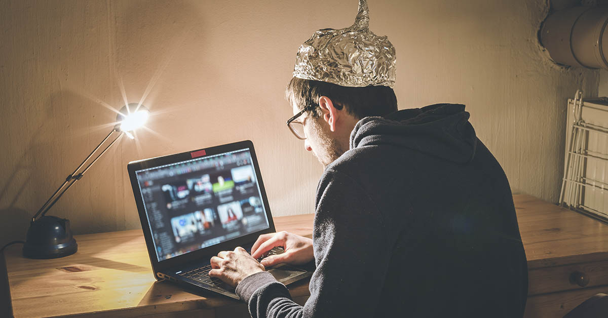 conspiracy theorist concept, man wearing tinfoil hat using laptop