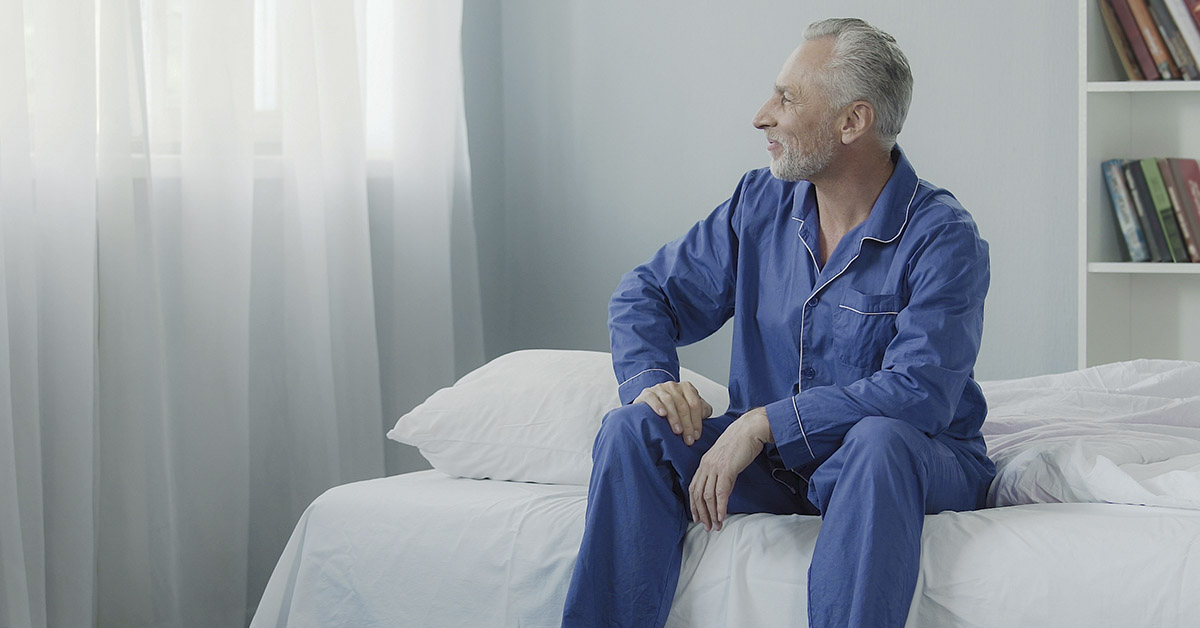 elderly man sitting on edge of bed in pajamas