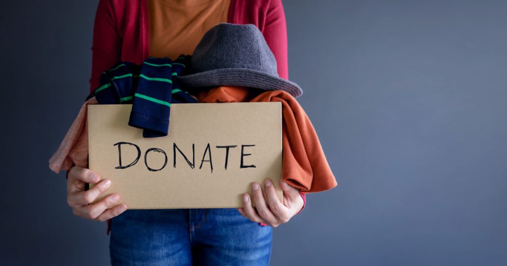 Donation Concept. Woman holding a Donate Box with full of Clothes
