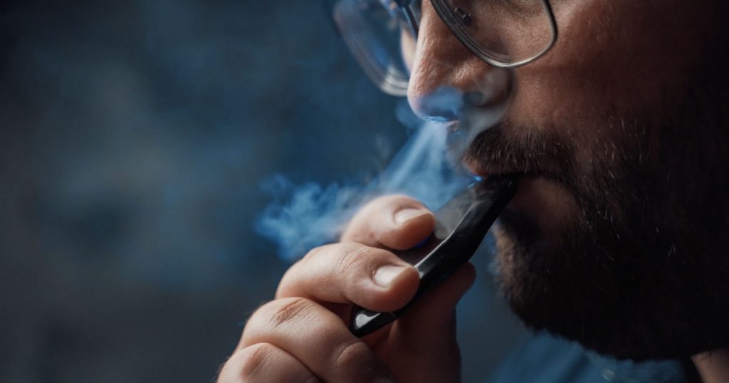 Man smokes new Vape Pod System, inhales and exhales vapor of electronic cigarette, vaping concept
