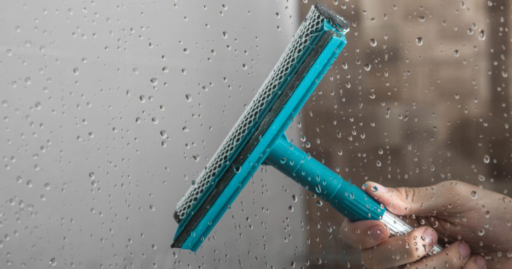 close up cleaning shower glass door with squeegee
