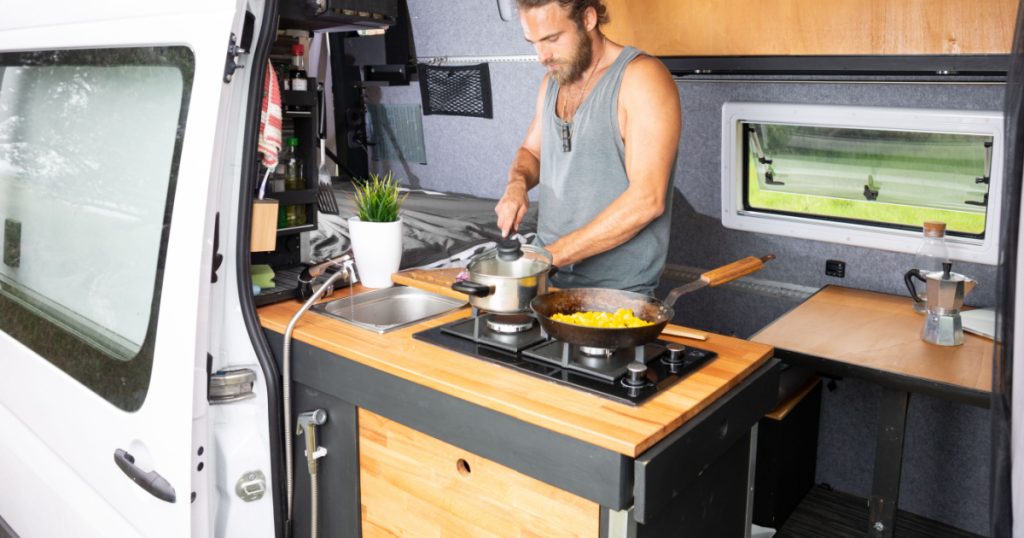 Man cooking in the kitchen area of his camper van
