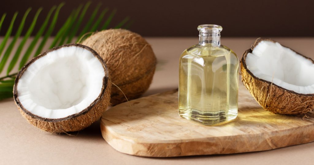 Bottle of coconut oil and fresh coconuts with palm leaf on wooden board over brown background. Coconut natural cosmetics.
