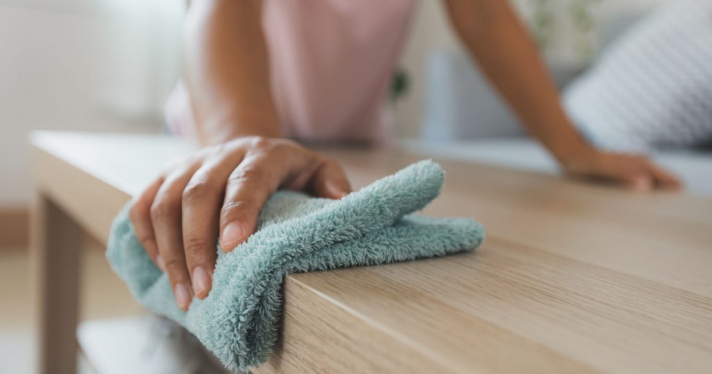 Woman cleaning and wiping the table with microfiber cloth in the living room. Woman doing chores at home. Housekeeping concept.
