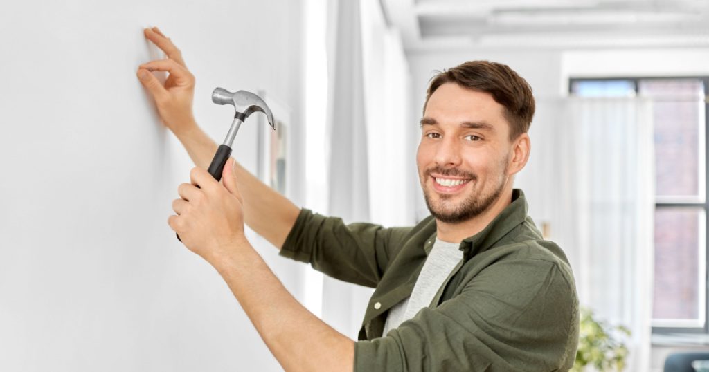 home improvement, repair and people concept - happy smiling man hammering nail to wall
