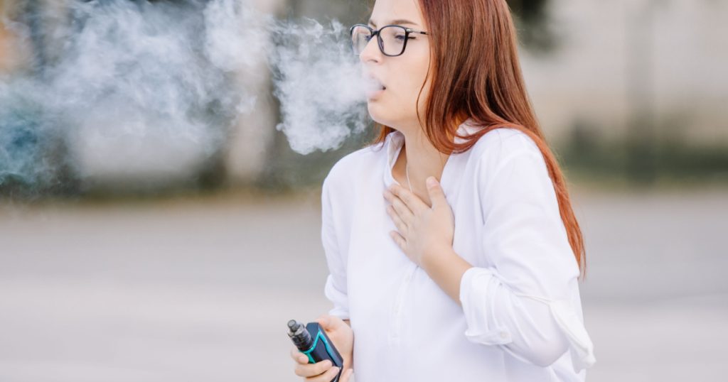 Young beautiful woman smoking vape coughing, suffering asthma or bronchitis. A woman struggling while smoking.
