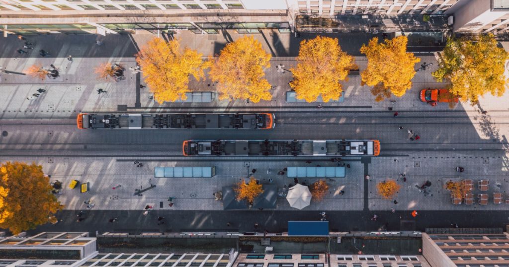 Aerial urban view above the German autumn street full of life with yellow trees squeezing between asphalt, city trams passing each other and people taking a walk or shopping. Mannheim, Germany.
