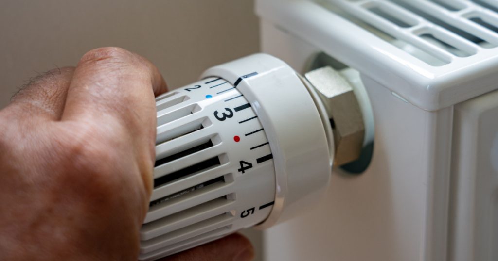 Rising heating costs in the crisis: Man regulates the temperature at home with the heating thermostat to save energy, close up with hand

