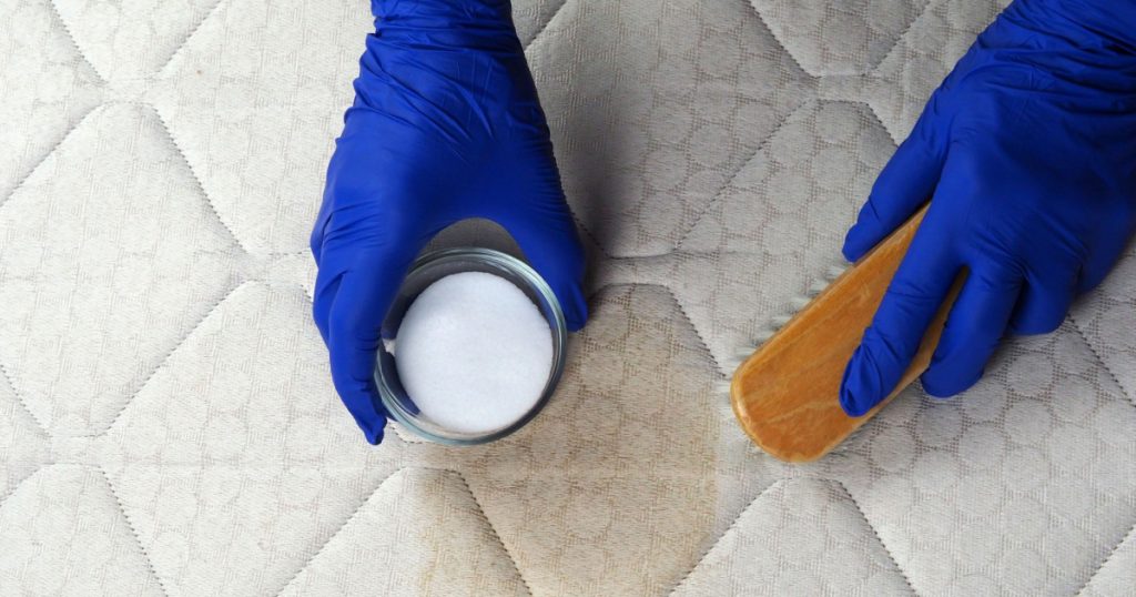 Hand cleaning surface of mattress on bed with brush and baking soda. Ecological cleaning and disinfection of surfaces. Hands in gloves do Mattress chemical cleaning. Copy space.
