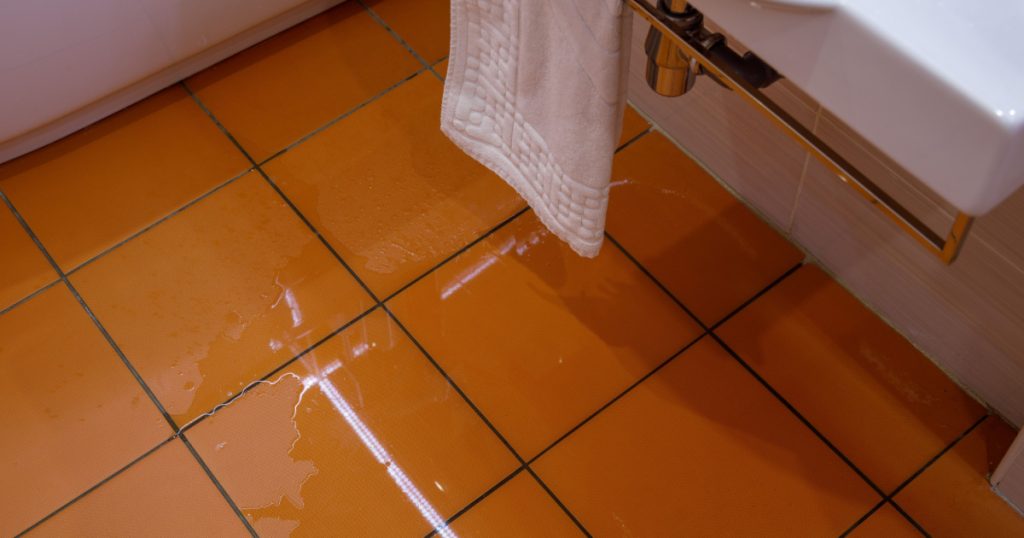 A puddle of water on the orange tiled floor in the room. Flooded production. Water leak in toilet or bathroom.
