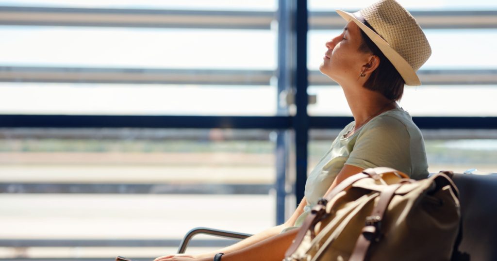 young asian female traveler with hipster backpack and hat at airport waiting for departure at Vienna Airport. Traveling woman relax , meditate and calm down before plane. flight fears concept

