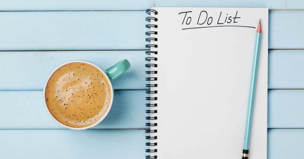 Coffee cup and notebook with to do list on blue rustic desk from above, planning and design concept
