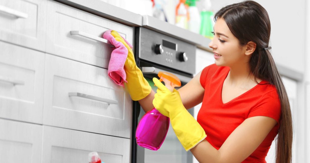 Beautiful woman in protective gloves cleaning kitchen cabinet
