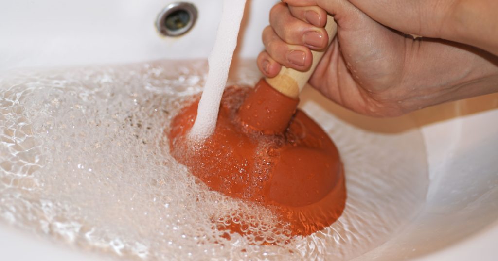 Woman with plunger trying to remove clogged sinks