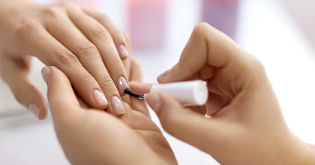 Nail Care And Manicure. Closeup Of Beautiful Female Hands Applying Transparent Nail Polish On Healthy Natural Woman's Nails In Beauty Salon. Manicurist Hand Painting Client's Nails. High Resolution
