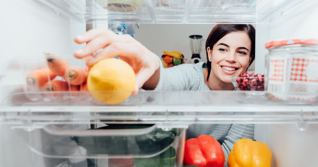 Smiling woman taking a fresh lemon out of the fridge, healthy food concept
