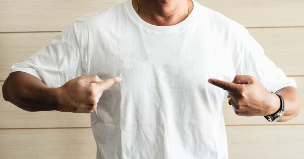 Smiling senior man show wearing white t-shirt on wooden background
