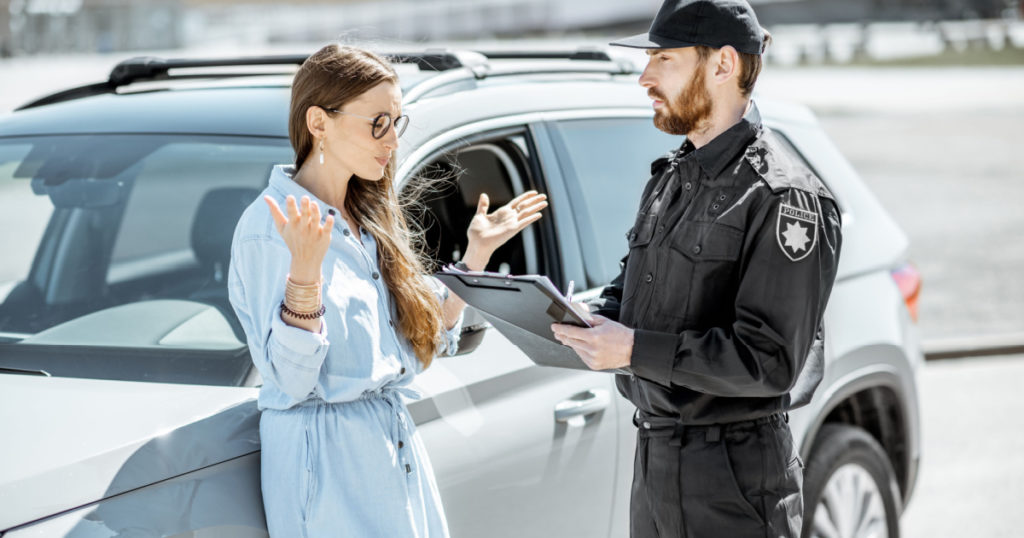 Policeman arguing with female driver while issuing fine for violating the traffic rules on the roadside near the car