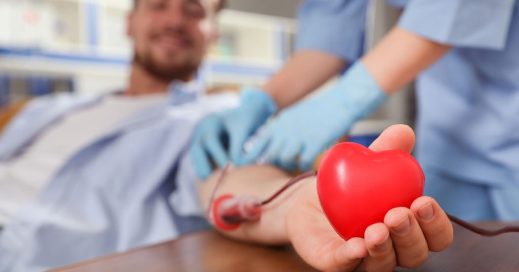 Young man making blood donation in hospital, focus on hand
