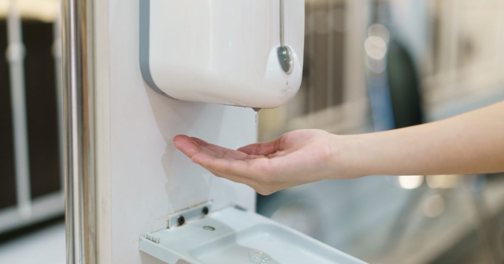 Hands with automatic sanitizer liquid spray machine, touchless dispenser.

